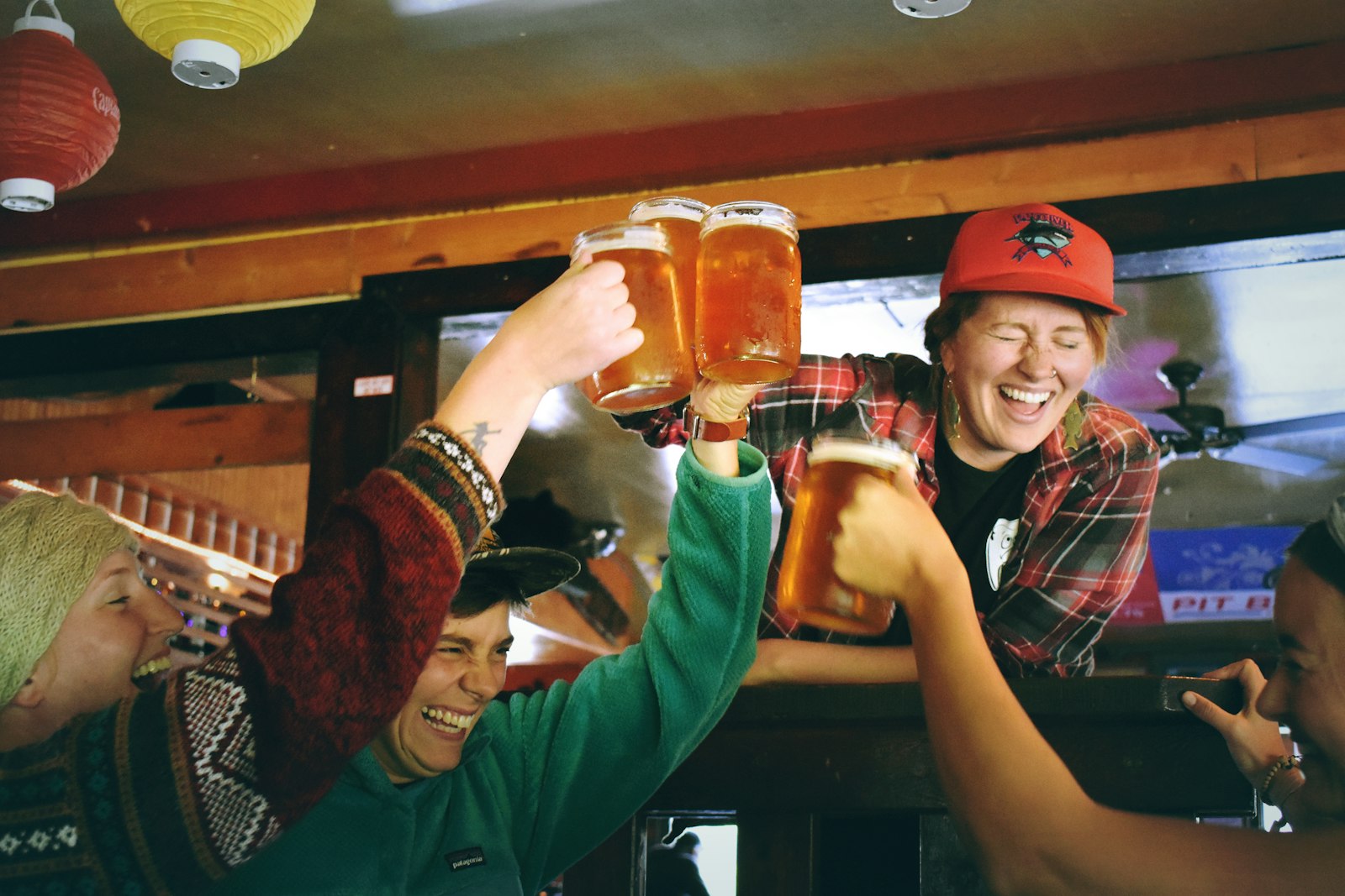 Group of friends toasting with beer mugs in a lively bar, smiling and laughing together.