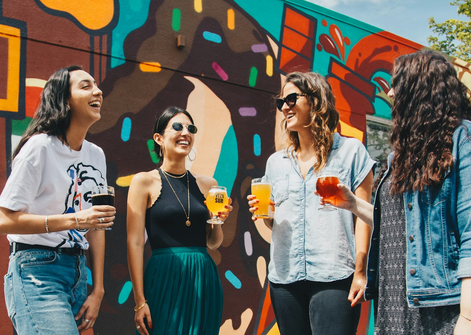 Four women laughing together with drinks on a girls trip
